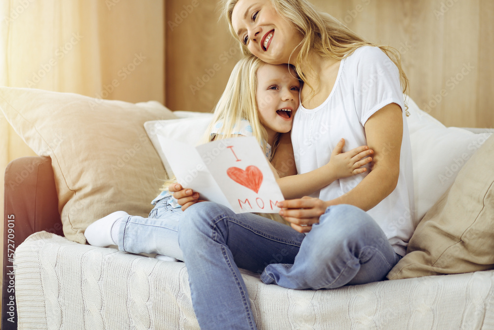 Happy mother day in sunny flat. Child daughter congratulates mom and gives her postcard with heart drawing. Family concept Happy mother day in sunny flat. Child daughter congratulates mom and gives her postcard with heart drawing. Family concept