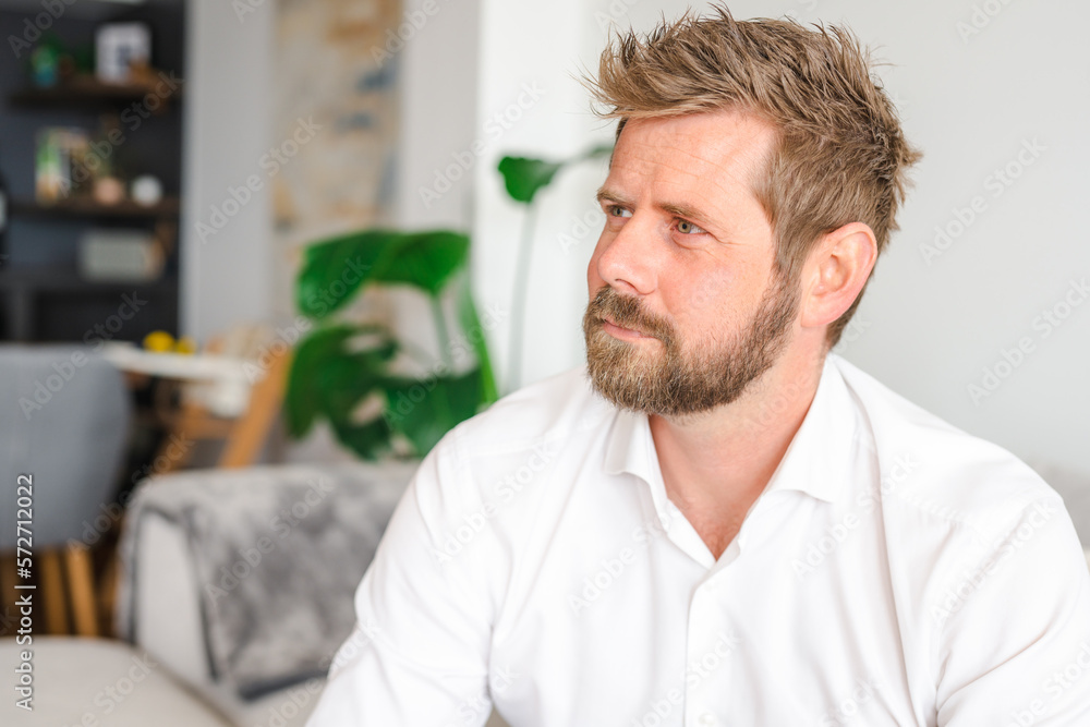 Successful confident young bearded blond adult male entrepreneur businessman professional in business casual clothes sitting at the modern home office and looking at camera Successful confident young bearded blond adult male entrepreneur businessman professional in business casual clothes sitting at the modern home office and looking at camera