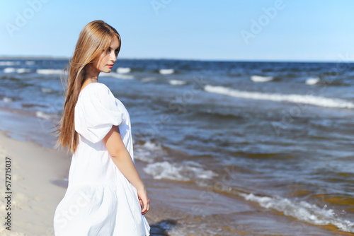 Happy, beautiful woman on the ocean beach standing in a white summer dress. Portrait