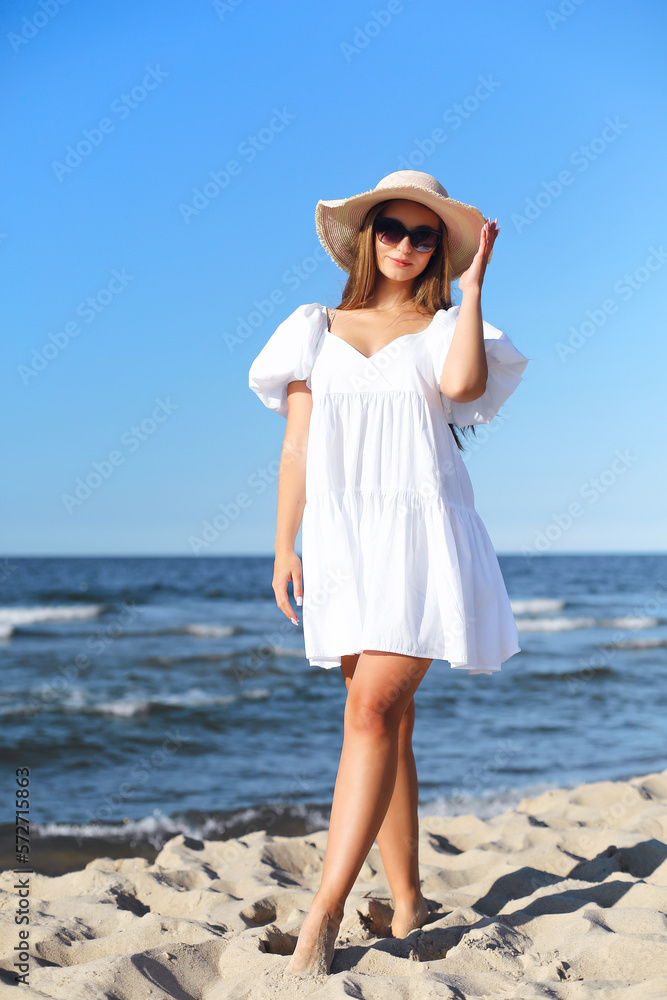 Happy smiling blonde woman is posing on the ocean beach with sunglasses and a hat Happy smiling blonde woman is posing on the ocean beach with sunglasses and a hat