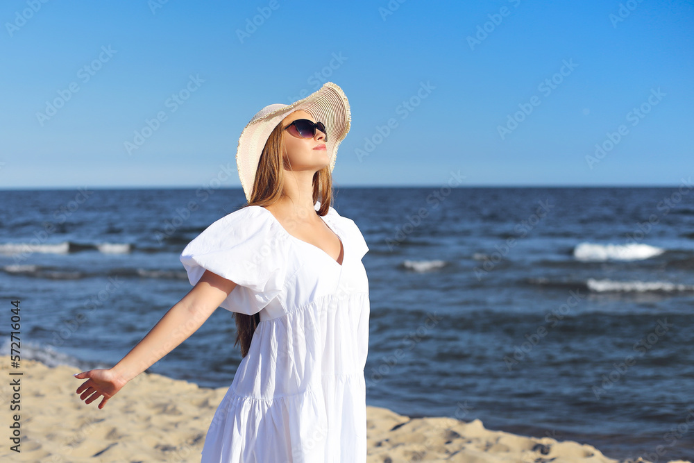 Happy blonde woman is on the ocean beach in a white dress and sunglasses, open arms Happy blonde woman is on the ocean beach in a white dress and sunglasses, open arms
