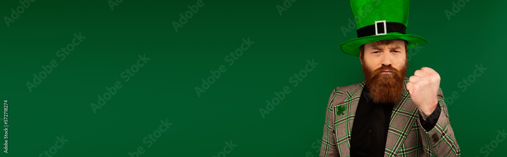 Angry man in hat and clover on jacket showing fist isolated on green, banner. Angry man in hat and clover on jacket showing fist isolated on green, banner.