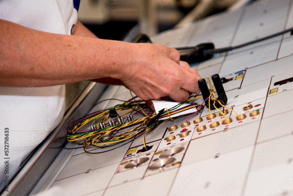 A worker in a production room with stands for manufacturing electric wiring for cars at a modern plant