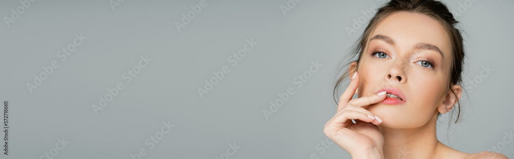 portrait of charming woman with natural makeup and hand near face looking at camera isolated on grey, banner. portrait of charming woman with natural makeup and hand near face looking at camera isolated on grey, banner.
