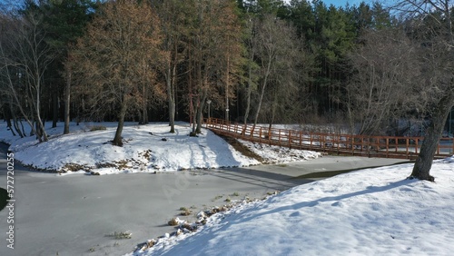 Suspension wooden bridge over an ice-covered river in the hydropark in winter. Swinging suspension bridge over water under a layer of snow. Winter health trail with a suspension bridge.