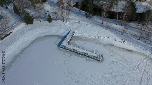 Berth under a layer of snow on the sea, lakes, rivers covered with ice. Pier for boats in winter under the ice. Coast in sub-zero cold in winter. Bank of the reservoir in winter.