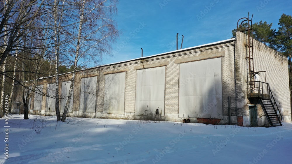 An abandoned building with boarded up and curtained windows stands in the middle of the forest in winter under a layer of snow. Soviet abandoned holiday camp for children and youth in winter. An abandoned building with boarded up and curtained windows stands in the middle of the forest in winter under a layer of snow. Soviet abandoned holiday camp for children and youth in winter.