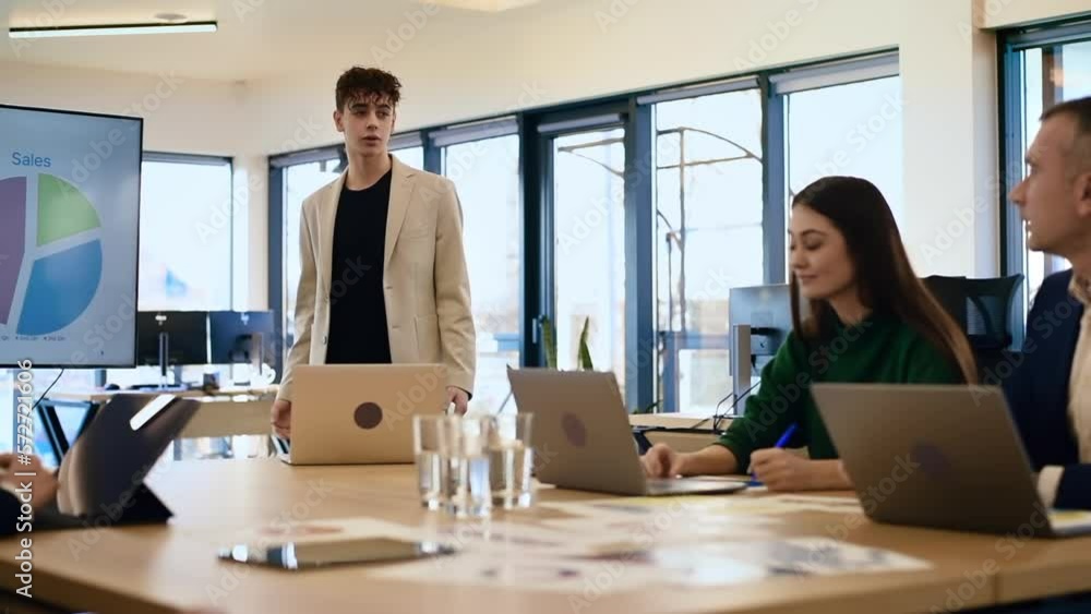 Young worker leading business meeting in an office, discussing business affairs with other workers using a big display with charts Young worker leading business meeting in an office, discussing business affairs with other workers using a big display with charts