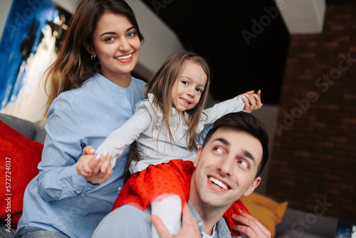 Father, mother and their daughter are smiling while spending time together. A day with family. Young happy couple with child playing at home.