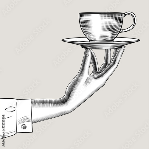 Female hand with a cup of tea or coffee on a saucer. Vintage engraving black and white stylized drawing. Vector illustration photo