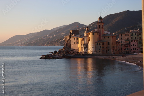 Camogli, Italy - January 27, 2023: Beautiful old mediterranean town at the sunset time with illumination during winter days. People enjoying the evening at the beach with beautiful sunset background