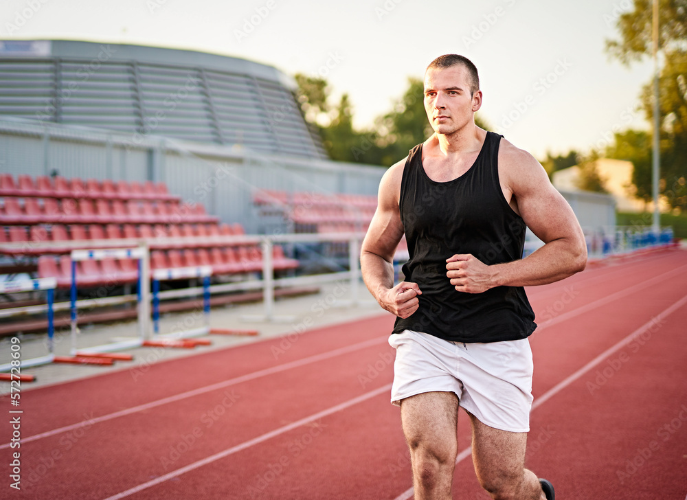 Young muscular fit male sprinter running on a red running track - Fitness and wellness concept with a millennial runner - Copyspace on the photo's left side