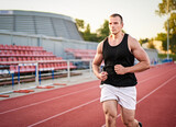 Young muscular fit male sprinter running on a red running track - Fitness and wellness concept with a millennial runner - Copyspace on the photo's left side