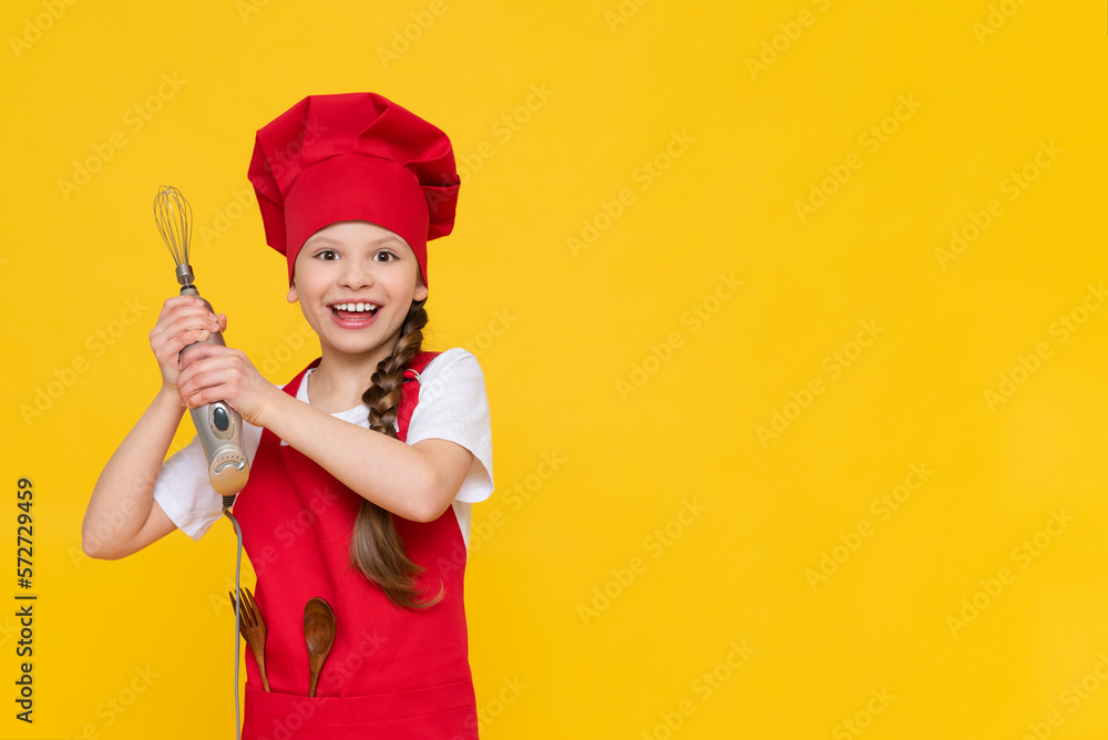 Chef little girl holds a blender for whipping. A child in a red cap and apron on a yellow isolated background. A place for advertising. Copy space. Chef little girl holds a blender for whipping. A child in a red cap and apron on a yellow isolated background. A place for advertising. Copy space.
