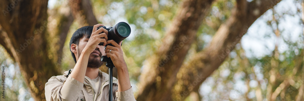 Asian man taking photo by camera enjoying camping outdoors in nature. traveling in the wild