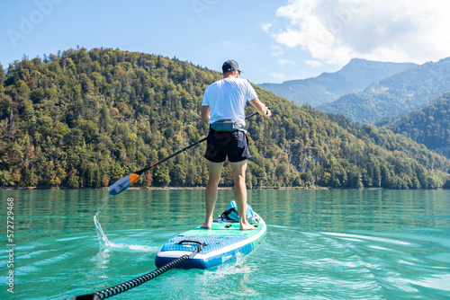 Athletic Man Paddling an Inflatable SUP Board in an Alpine Lake