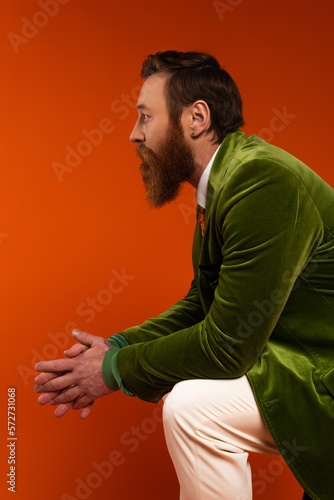 Side view of bearded man in stylish green blazer looking away on red background. © LIGHTFIELD STUDIOS