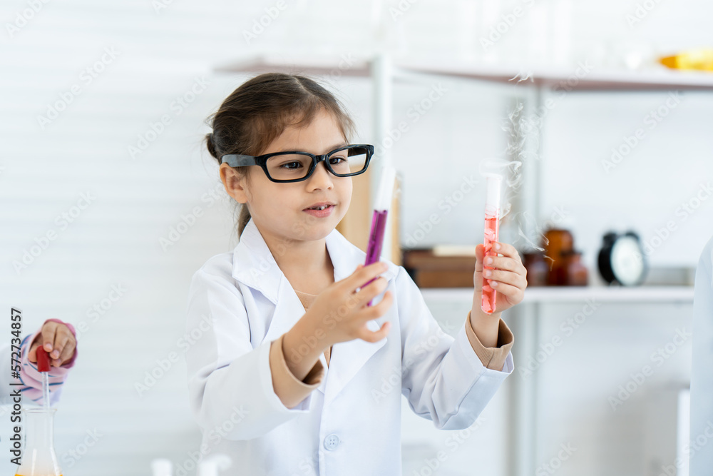 A little Arab girl in glasses in the role of a scientist is paying attention to the color in the test tube in the science classroom. elementary school chemistry science experiment A little Arab girl in glasses in the role of a scientist is paying attention to the color in the test tube in the science classroom. elementary school chemistry science experiment