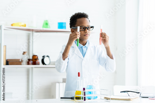 African Little boy guessing and wondering colorful liquids in test tubes in both hands in white elementary school science laboratory. education, science experiment, chemistry,