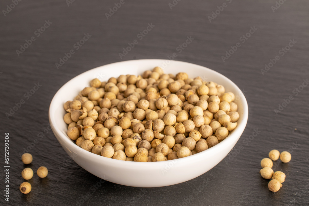 Fragrant vegetable coriander seeds in white plate on slate stone, macro. Fragrant vegetable coriander seeds in white plate on slate stone, macro.