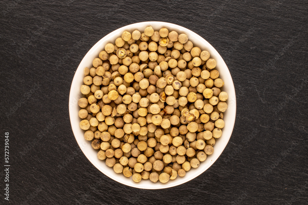 Fragrant vegetable coriander seeds in white plate on slate stone, macro, top view. Fragrant vegetable coriander seeds in white plate on slate stone, macro, top view.