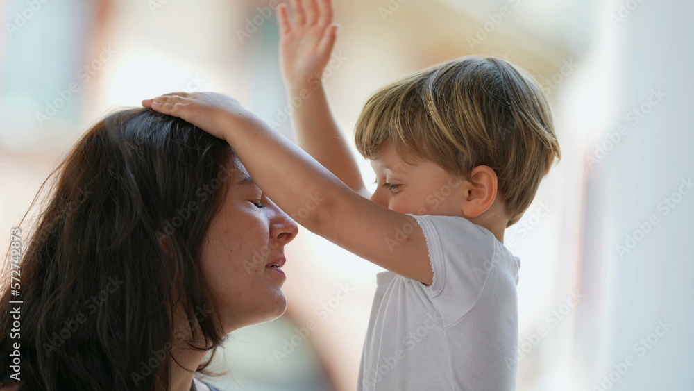Naklejka premium Parenting stress. Patient mother. Little boy hitting parent in the head with hand. Child misbehavior outside. Lifestyle real life stressful moment