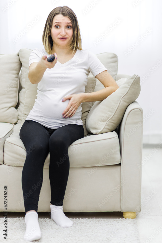 Photo of pregnant young woman with remote control in hand. Photo of pregnant young woman with remote control in hand.