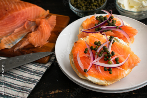 Sliced Bagel Topped with Lox, Onion, Capers, and Cream Cheese: Slices of cured salmon with various toppings on a plain bagel