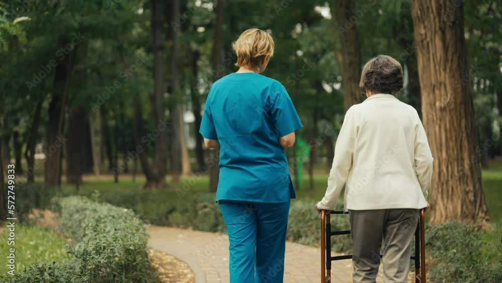 Female nurse keeping company to senior woman with disability walking in park Female nurse keeping company to senior woman with disability walking in park