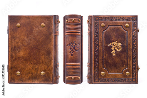 Aged brown leather book with the Eye of Horus in the center of the front cover and the book spine. The cover is embossed, gilded, have metal corners, raised ribs on the spine. 