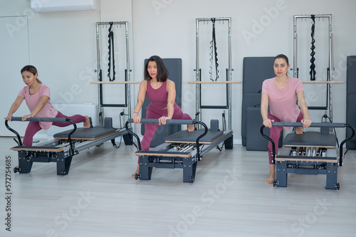 Three Asian women in pink sportswear do exercises on the reformer machine. Pilates classes.