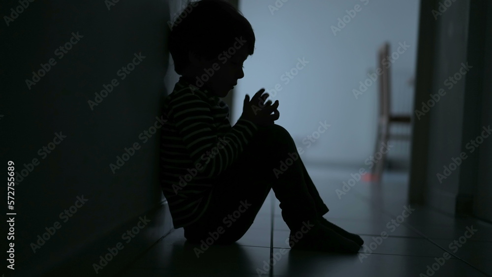 Small child covering face feeling despair. One small boy sitting in dark hallway corridor at home suffering alone in crisis