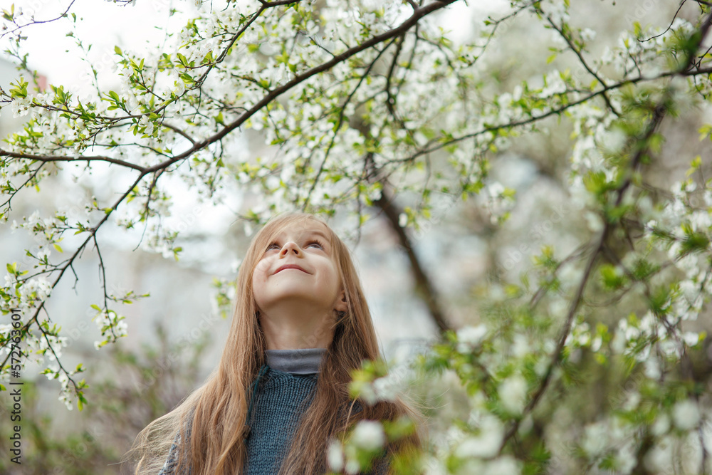 Cute cheerful happy smiling little girl under blooming cherry tree with white flowers looking up in spring park or garden on sunny day, cozy warm child portrait, tenderness and happiness of childhood Cute cheerful happy smiling little girl under blooming cherry tree with white flowers looking up in spring park or garden on sunny day, cozy warm child portrait, tenderness and happiness of childhood