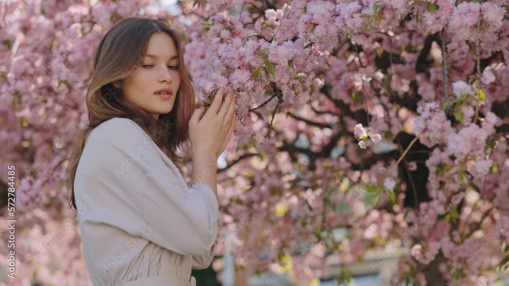 Attractive Girl Looking at Camera While Standing Near Beautiful Spring Blossom of Sakura Tree. People Portrait. Leisure Time Spending on Fresh Air Attractive Girl Looking at Camera While Standing Near Beautiful Spring Blossom of Sakura Tree. People Portrait. Leisure Time Spending on Fresh Air