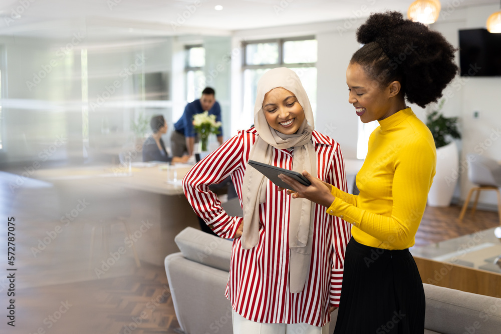 Happy diverse businesswomen with tablet working and talking in office Happy diverse businesswomen with tablet working and talking in office