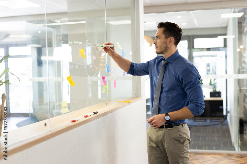 Focused caucasian man working and writing on glass board in office Focused caucasian man working and writing on glass board in office