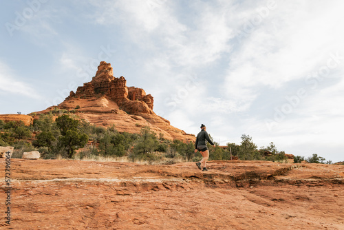 Woman hiker standing on Bell Rock trail in red rock formations within coconino national forest in Sedona Arizona USA against white cloud background.