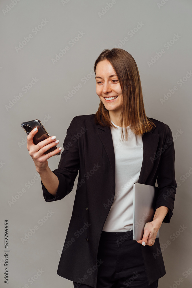 Smart smiling woman wearing jacket is holding a laptop and her cellphone. Smart smiling woman wearing jacket is holding a laptop and her cellphone.