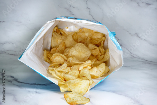 Bag of potato chips laying on counter with chip falling out photo