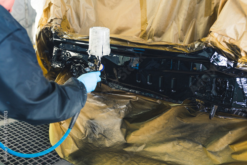 Foto Auto mechanic wearing gloves painting a car in a repair shop using an airbrush