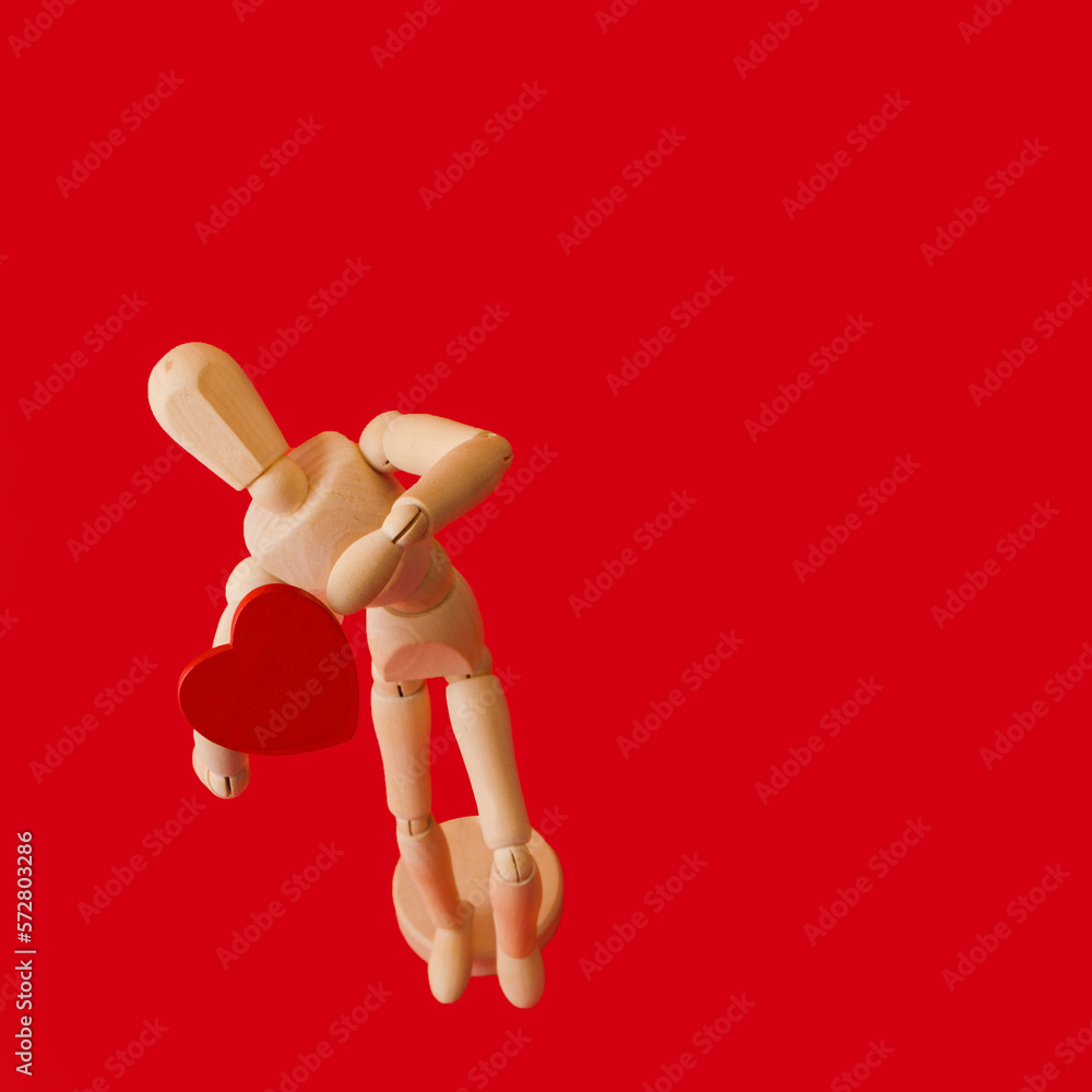 Wooden man with a heart in his hands on a red background Wooden man with a heart in his hands on a red background