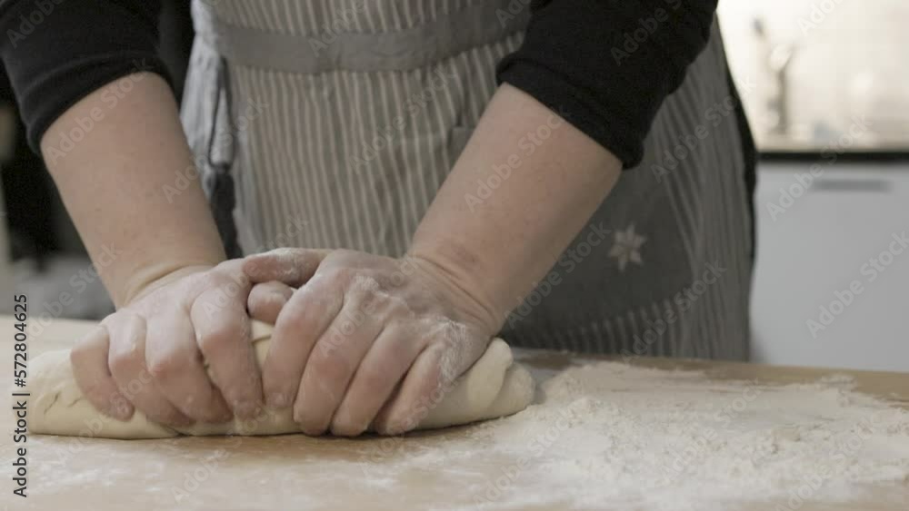 Woman with apron kneads a bread dough on an old vintage baking table Woman with apron kneads a bread dough on an old vintage baking table
