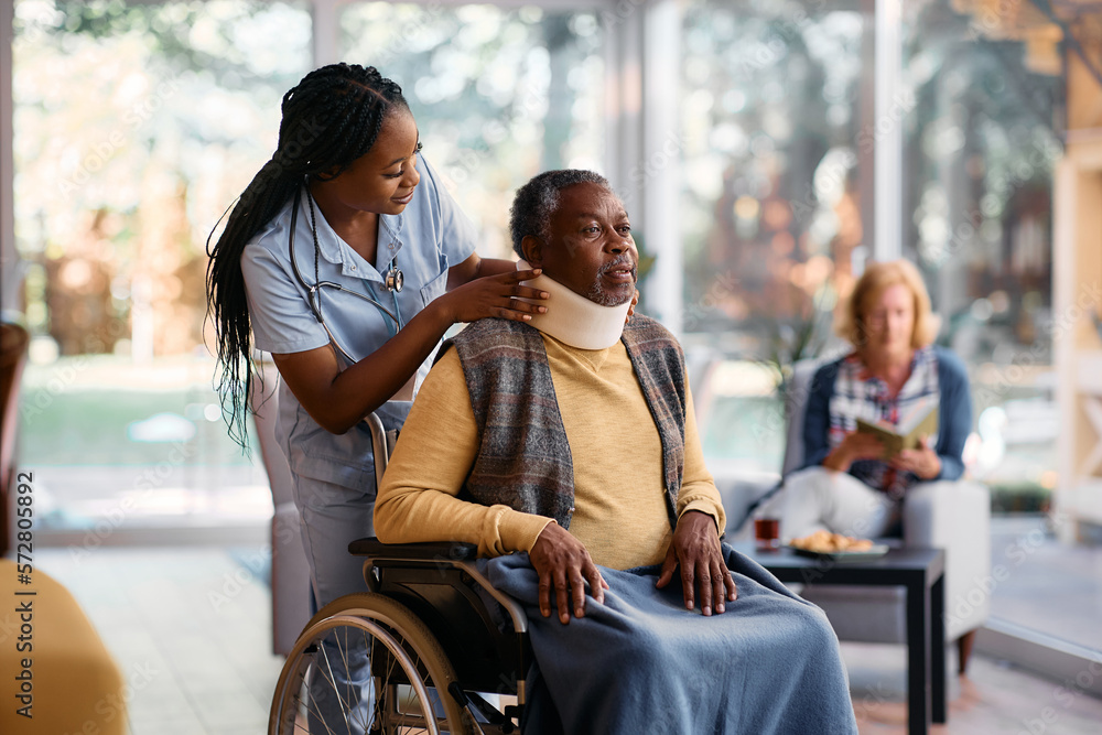 Young black nurse putting cervical collar on senior man's neck at nursing home. Young black nurse putting cervical collar on senior man's neck at nursing home.