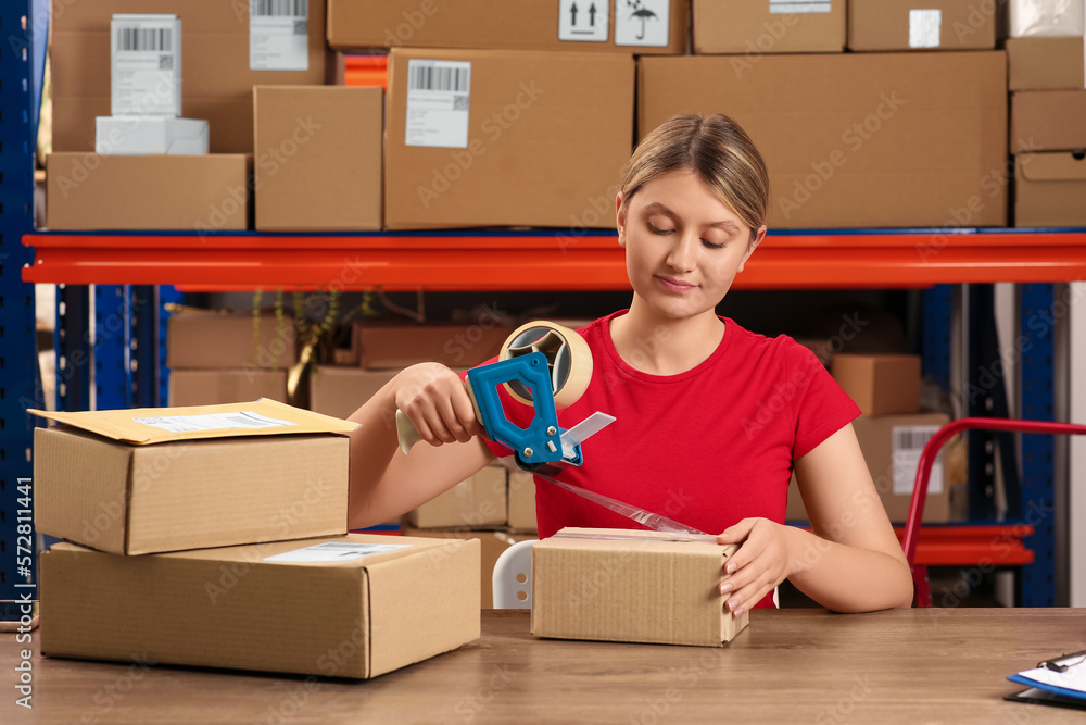 Post office worker packing parcel at counter indoors