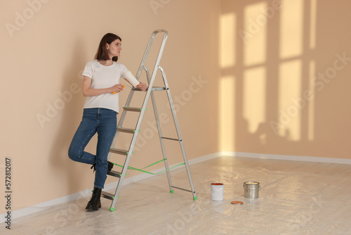 Young woman with roller near metal stepladder indoors. Room renovation