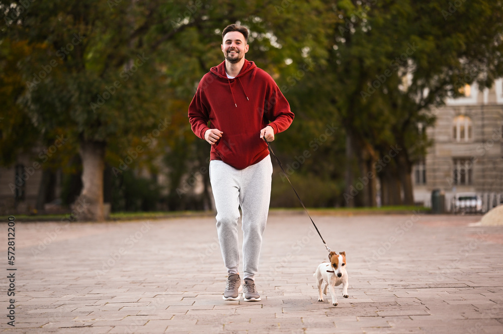 Obraz premium Man running with adorable Jack Russell Terrier on city street. Dog walking