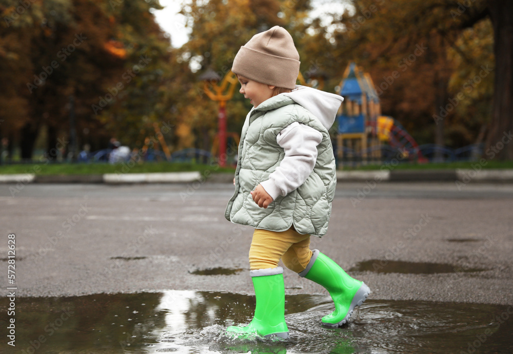Cute little girl splashing water with her boots in puddle outdoors Cute little girl splashing water with her boots in puddle outdoors