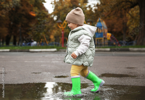 Fototapeta Naklejka Na Ścianę i Meble -  Cute little girl splashing water with her boots in puddle outdoors