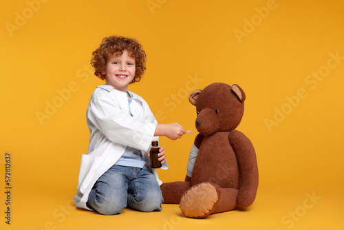 Little boy playing doctor with toy bear on yellow background