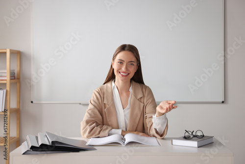 Happy young teacher explaining something at table in classroom